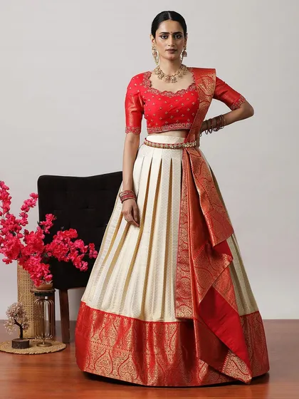 An elegant cream and red lehenga, featuring a pleated skirt and a rich Banarasi border and dupatta. A classic South Indian style.