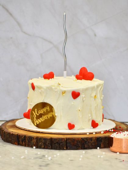 A simple and heartfelt anniversary cake. This design features a rustic buttercream finish, scattered red hearts, and a gold "Happy Anniversary" plaque.