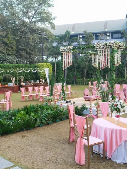 An overview of the entire outdoor wedding venue, showing the mandap, guest seating, and buffet area. The consistent pink and green color scheme ties the whole event space together beautifully.