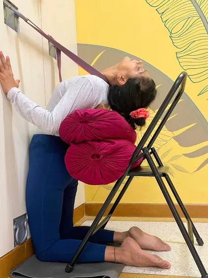 This supported Ustrasana (Camel Pose) uses a chair, bolsters, and a wall rope. The props work together to create traction and support, allowing for a deep, passive opening of the chest and shoulders.