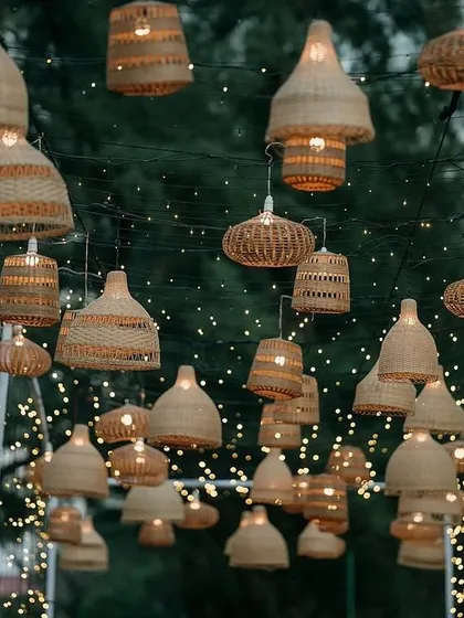 A video tour of a magical entry pathway for a beachside event. The walkway is lined with fairy lights and features an overhead installation of hanging wicker lamps, creating a starry night effect.
