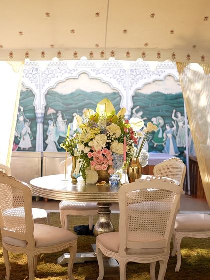 An intimate seating arrangement inside a tented area at the Mehendi. The backdrop features a beautiful hand-painted mural, adding a touch of local artistry to the decor.