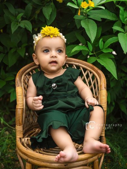 A close-up shot of the baby girl against a lush green foliage background. The vibrant natural colors make for a stunning and timeless portrait.