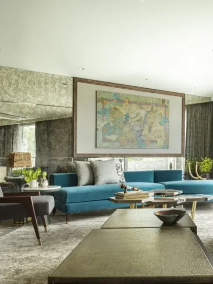 The formal living room at the Jor Bagh Residence, featuring a mix of custom sofas in teal and grey. A large piece of art is recessed into the wall, creating a focal point that is integrated with the architecture.