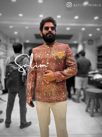 A client in a brocade Jodhpuri jacket featuring a rich red and gold paisley pattern. Paired with off-white trousers, this look is perfect for a wedding guest or festive celebration.
