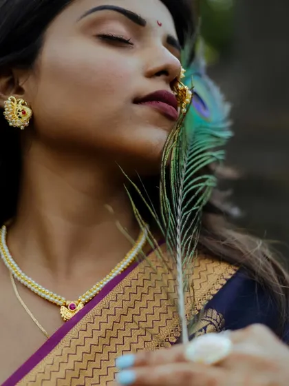 A creative close-up using a peacock feather as a prop. This artistic portrait highlights the model's traditional jewelry and the rich texture of her saree, creating a connection to cultural symbolism.