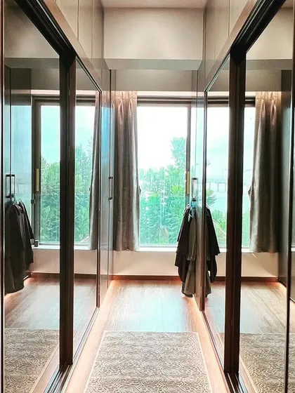 Another view of the walk-in wardrobe, where the reflections in the mirrored doors capture the natural light from the window at the far end.