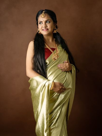 A classic three-quarter portrait of a mom-to-be in a stunning green silk saree and traditional jewelry, looking radiant.