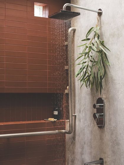 A skylight brings a "shower of light" into the bathroom. The walls are finished in a monotone cement oxide, with an accent wall of terracotta tiles that absorbs the light and defines the volume of the space.