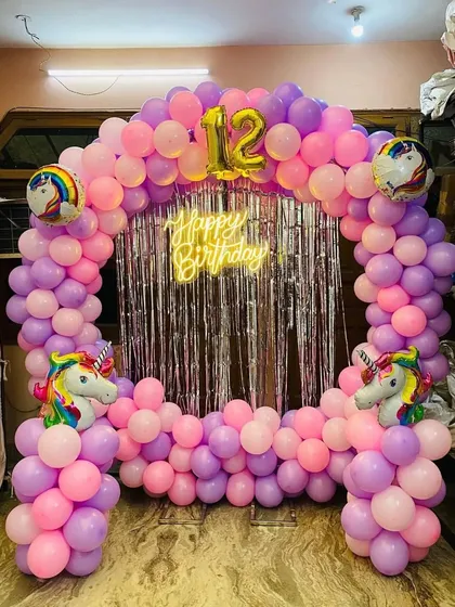 A straight-on view of the unicorn party backdrop, featuring a neon 'Happy Birthday' sign and number '12' foil balloons.