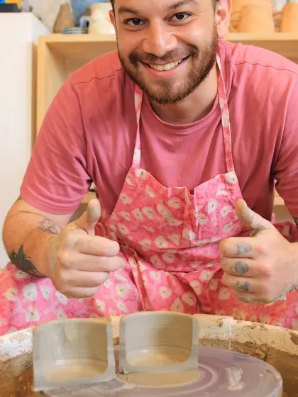 A happy student gives a thumbs up from the pottery wheel, proud of the two cylinders he has just thrown.