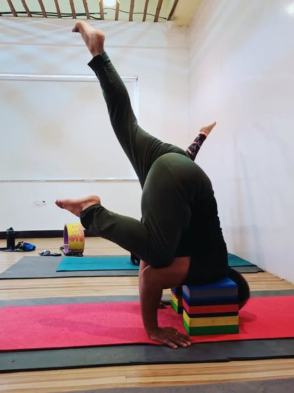 A student practices an advanced arm balance, a variation of Pincha Mayurasana, using blocks for support. This helps to build stability and confidence in inversions.