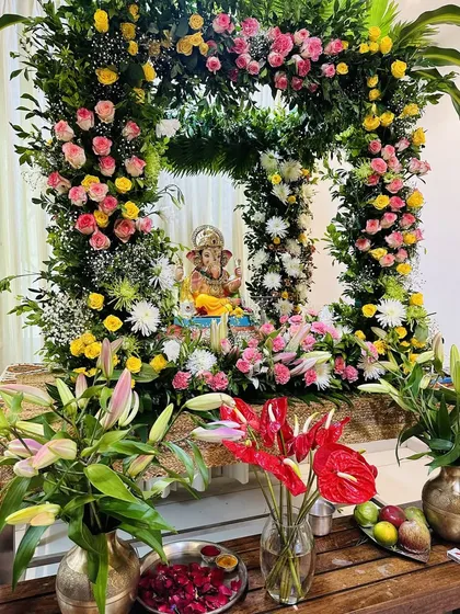This vibrant Ganpati mandap is crafted from a mix of fresh flowers, including pink and yellow roses, lilies, and anthuriums. The full floral arch creates a beautiful and auspicious frame for the idol.