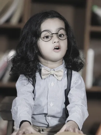 A thoughtful black and white portrait of a young boy with glasses, giving him a wise and studious look.