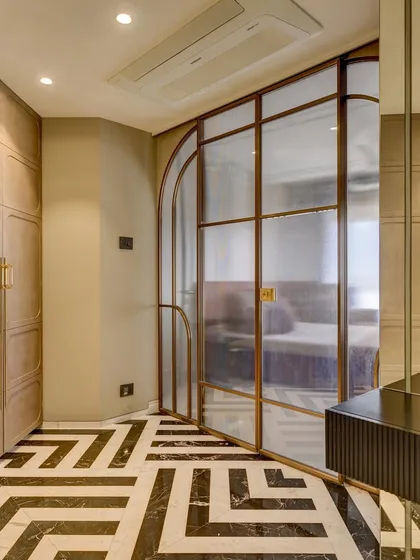 A view into the master bedroom from the walk-in wardrobe. The arched glass door and monochrome flooring create a grand transition between the two spaces.