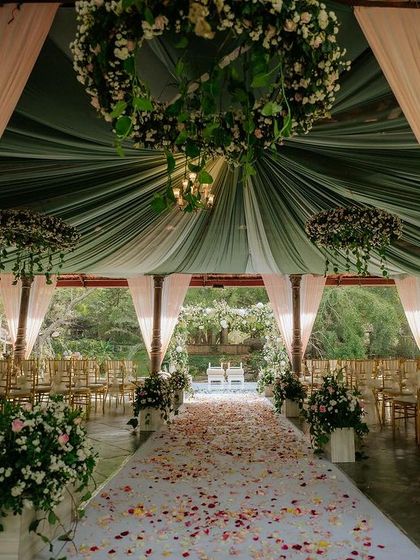 A beautiful aisle runner of scattered petals leads to the mandap, which is draped in pastel green and pink fabrics.