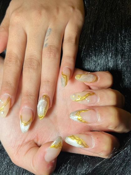 A dramatic set of long, clear extensions with bold, 3D gold chrome swirls and a silver glitter base.