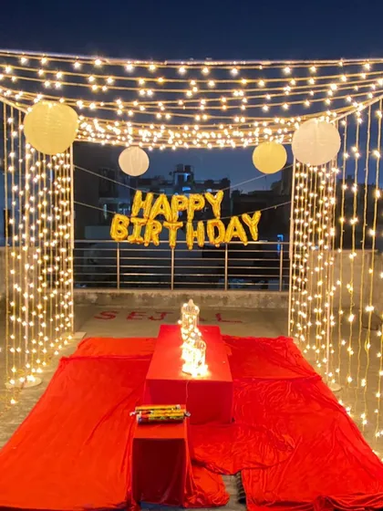 A vibrant terrace decoration with red floor coverings, low seating, and a ceiling of fairy lights, creating a warm and inviting space for a birthday.