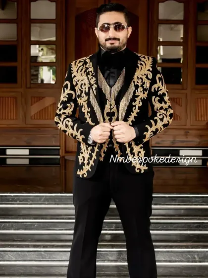 A groom wearing a custom black tuxedo with elaborate gold embroidery and fringe detailing. This is a maximalist design for those who want to make a grand statement.