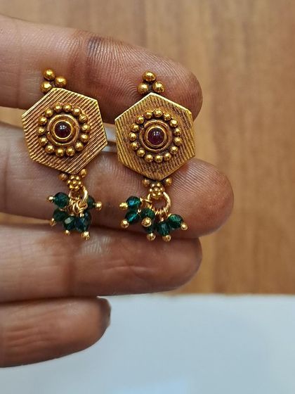 A pair of hexagonal antique gold-plated earrings with a central stone and green bead drops. These are a unique and stylish choice for daily wear.