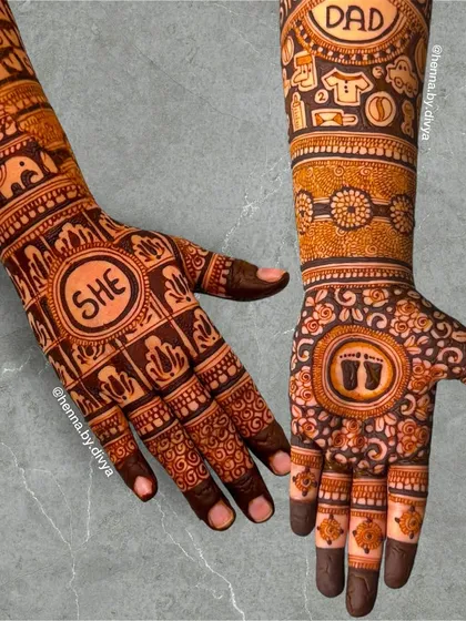 A fun gender reveal mehendi design. One arm features the word 'SHE' and the other 'DAD', with baby footprints and other cute symbols to celebrate the coming of a baby girl.