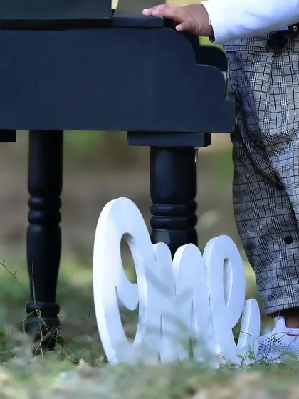 A detail shot from a first birthday session, focusing on the "One" sign placed next to the miniature piano prop.