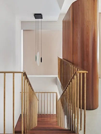 Looking down the stairwell, the brass railings and curved wooden wall create a dynamic composition of lines and forms. A modern pendant light hangs in the void, adding another layer of sculptural interest.