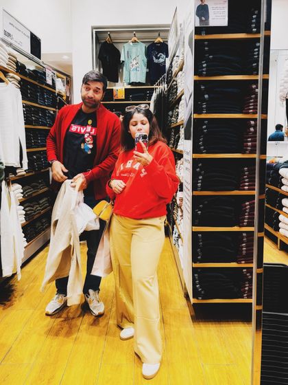 A fun mirror selfie during a winter shopping trip. My cozy red sweatshirt and tan trousers make for a comfortable and festive look, even if my husband tries to photobomb.