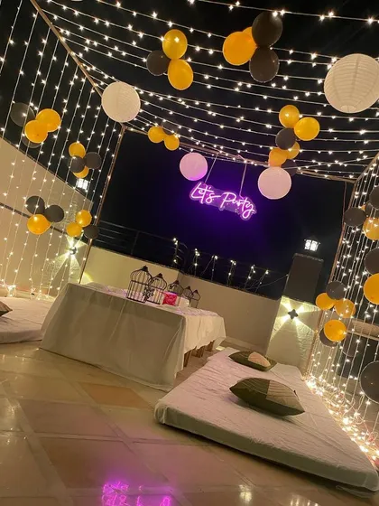 This is a duplicate of ID 34, 45, 79, 99, 125. A relaxed and stylish terrace party setup. This decoration features a canopy of fairy lights and paper lanterns, with low seating arrangements and a 'Let's Party' neon sign.
