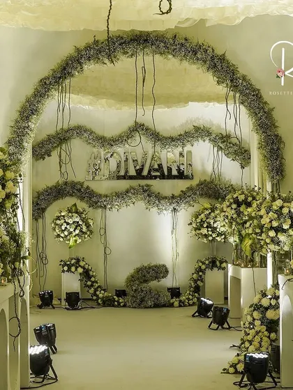 The main photo backdrop, with the couple's hashtag in mirror letters, set against a wall of white and green florals and hanging baby's breath.
