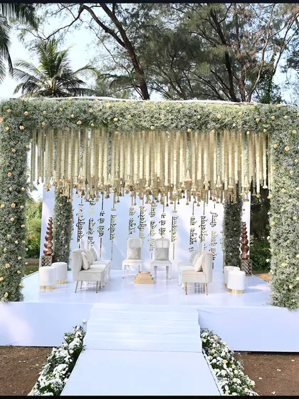 A detailed look at the pristine white mandap at ITC Goa, framed by lush greenery. The hanging floral strings and clean white stage create a heavenly atmosphere.