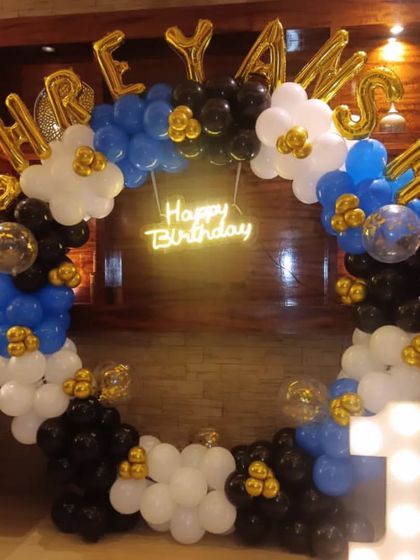 A balloon ring decoration in blue, black, and white for a first birthday, personalized with foil letters for the name.
