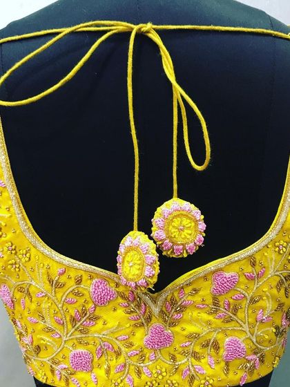 A yellow blouse with delicate pink heart-shaped floral embroidery. The back has a deep V-cut, and the latkans are custom-made to match the embroidery design.