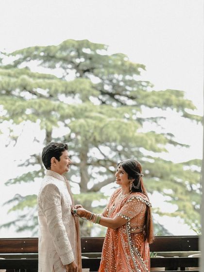 A tender moment between the couple with a large, beautiful tree as their backdrop. The bride adjusts the groom's outfit, a small, intimate gesture that speaks volumes about their care for each other.