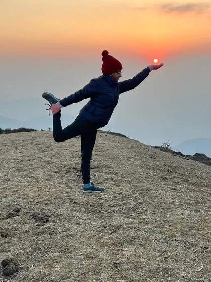 Holding Natarajasana, the lord of the dance pose, as the sun sets over the mountains during a trek. This pose is a beautiful expression of balance and grace, and practicing it in nature's embrace brings a profound sense of peace and connection to the end of the day.