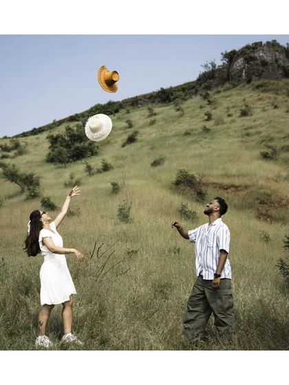 A fun, action shot of a couple playing with hats in a grassy field, capturing their playful energy.