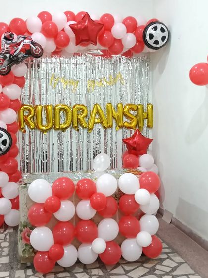 A motorcycle-themed birthday decoration with a red and white balloon arch, wheel and star foil balloons, and a silver curtain backdrop.