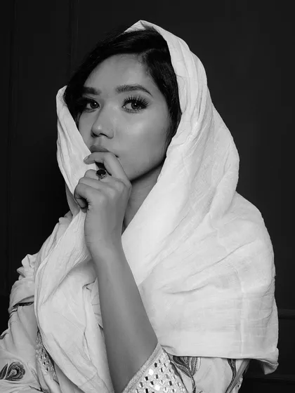 A classic portrait in black and white, with the model's face partially covered by a white scarf. This creates a sense of mystery while highlighting her striking eyes.