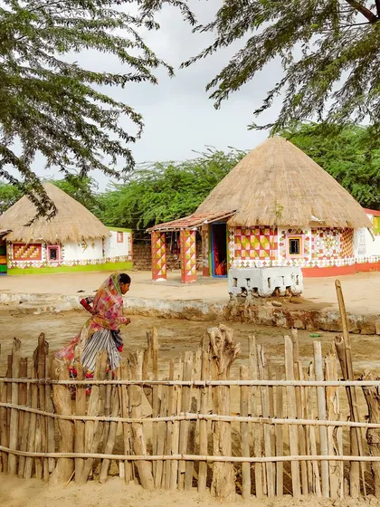 A Meghwal woman walks past traditional Bhunga huts in her village in Kutch. This environmental shot captures the harmony between the people, their art, and their surroundings.