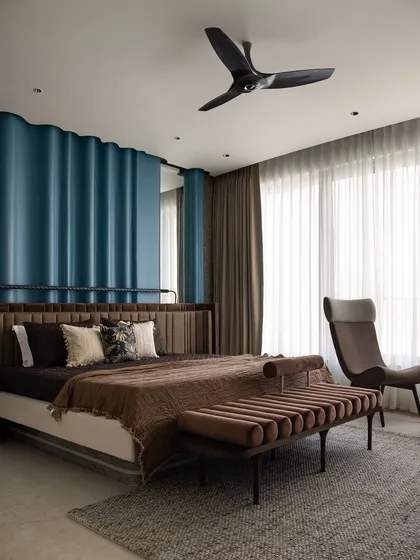 In this spacious master bedroom, we wanted to create a serene retreat. The statement blue ripple paneling behind the bed adds texture and drama, while the custom-designed upholstered bed, ottoman, and lounge chair ensure comfort. This space is a testament to our belief in creating uncluttered, elegant, and highly personalized rooms.