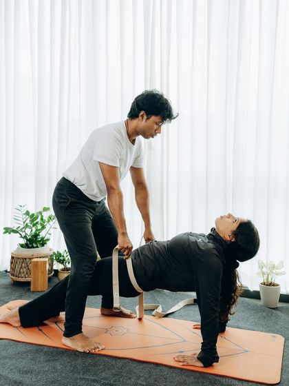 An instructor uses a strap to assist a student in Purvottanasana (Upward Plank), showcasing how partner guidance can enhance a pose.