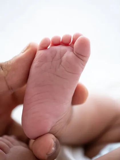 A parent's thumb gently holds a tiny foot, showing the incredible scale and sweetness of a newborn's features.