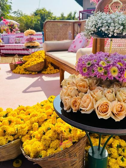 A modern twist on Haldi decor with tiered floral stands featuring roses and chrysanthemums, alongside traditional baskets of marigolds.