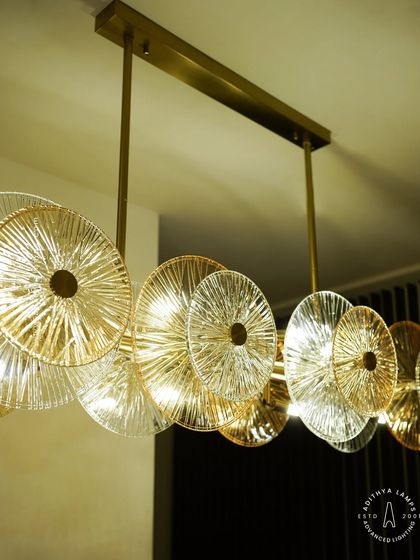 A linear chandelier featuring an arrangement of clear and amber-tinted textured glass discs. This fixture provides both direct and ambient light, adding a layer of sophistication and warmth to dining areas and boardrooms.