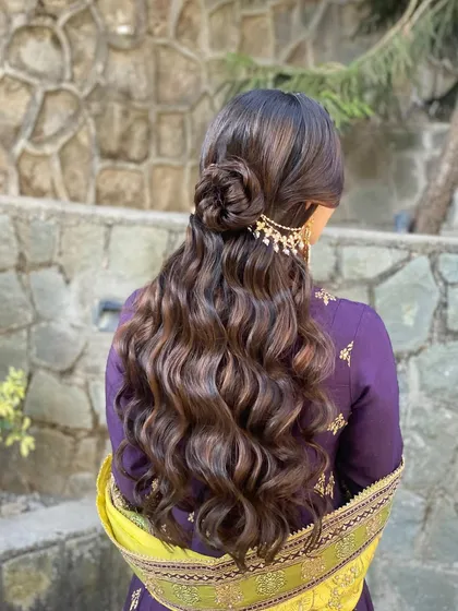 A half-up style with a rose bun and soft waves for a Mehendi look. The combination of the floral element and flowing curls is both romantic and chic.
