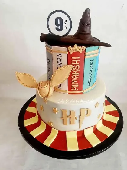 A truly magical Harry Potter cake for a 9th birthday. This two-tier design features hand-painted books, an edible sorting hat, a magic wand, and the golden snitch, all crafted with minimal fondant for a great taste.