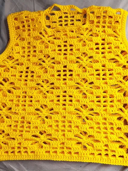 A flat-lay of the Argalia Bloom Top, showcasing the detailed craftsmanship and the vibrant yellow yarn before it's worn.