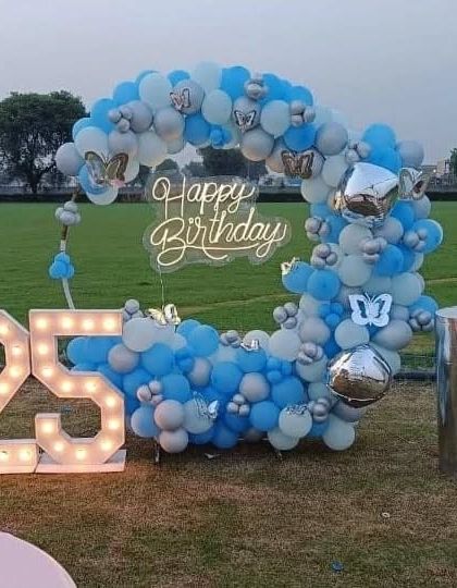 An outdoor 25th birthday party with a blue and silver balloon ring and marquee numbers.