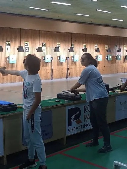 A coach provides guidance to a young shooter during a practice session. This personalized attention ensures that each athlete develops the correct technique for holding, aiming, and firing the pistol.