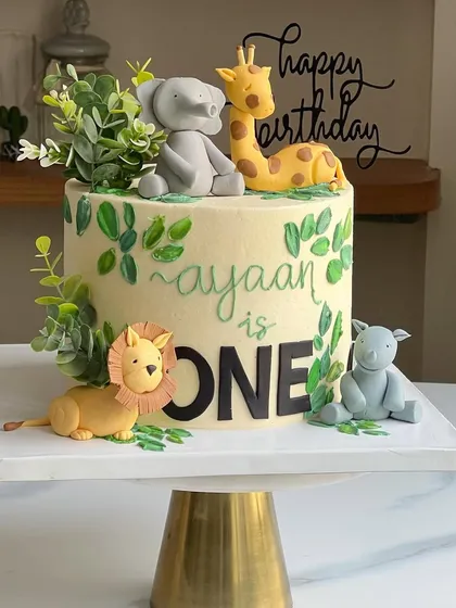 A sweet and simple jungle-themed first birthday cake. This buttercream cake is decorated with hand-painted leaves and topped with adorable fondant safari animals.